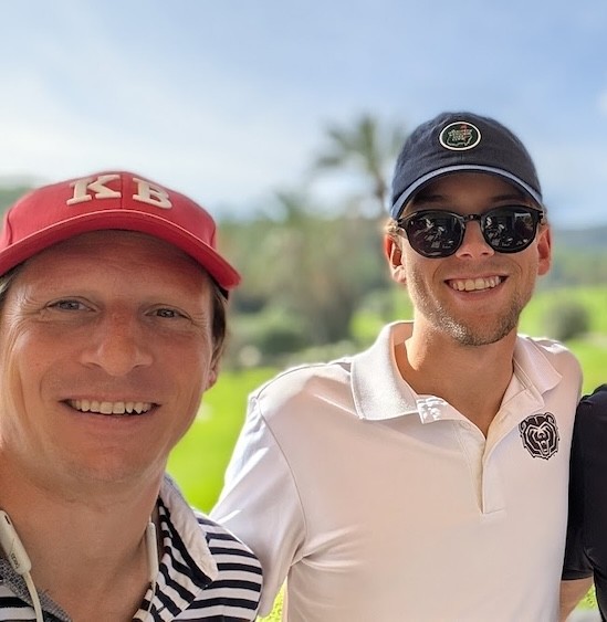 A tranquil canal in Amsterdam reflects historic buildings and the autumn-colored trees under a pastel sky with birds flying above; capturing the serene beauty and cultural architecture of the city.