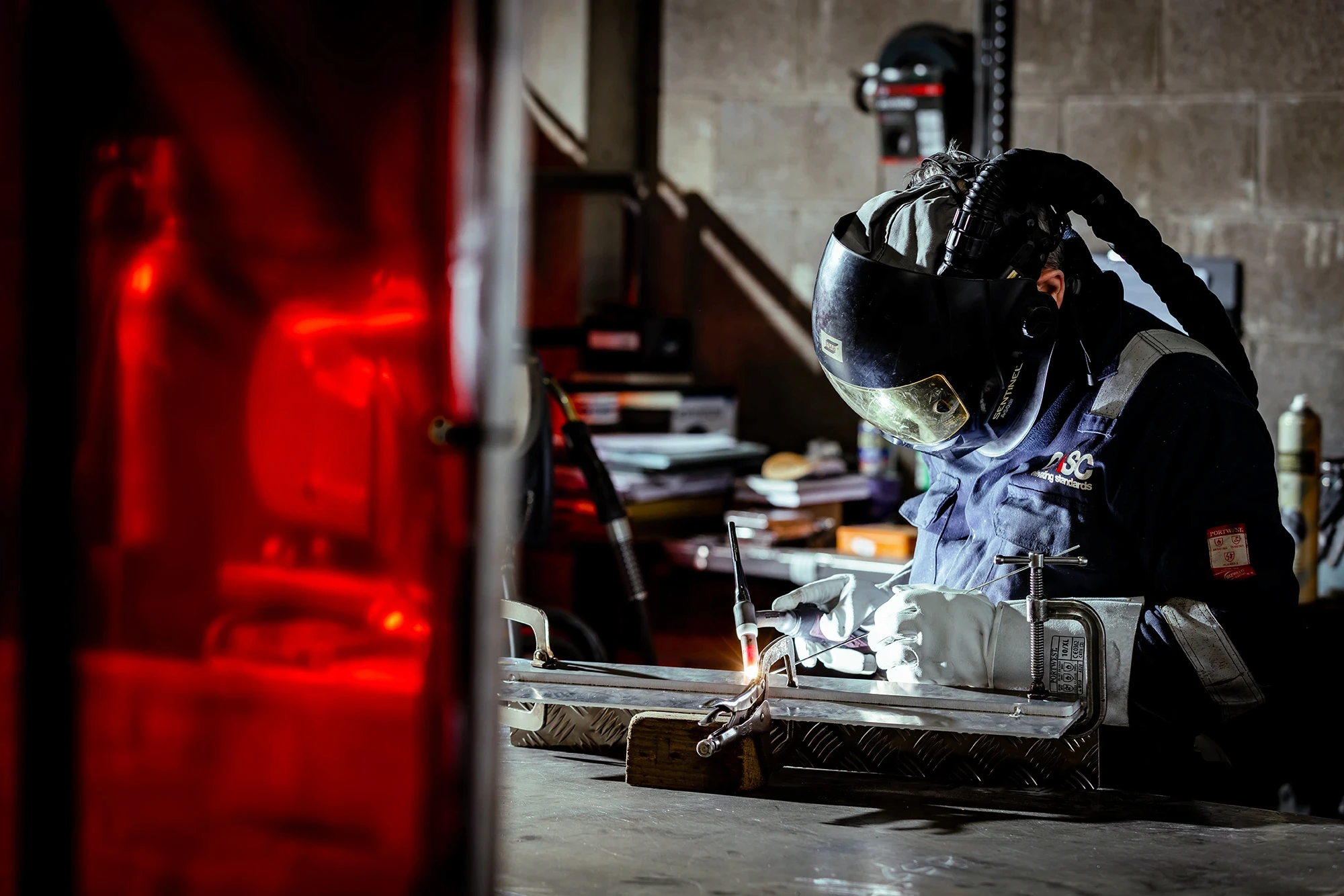 Skilled fabricator TIG welding a metal component in a workshop, wearing protective gear during precision welding and fabrication work.
