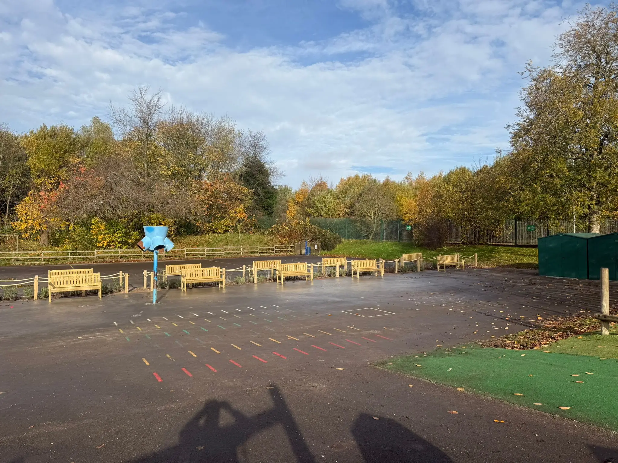 A park scene with benches and trees under a partly cloudy sky, showcasing a tranquil outdoor setting.
