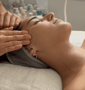 A luxurious bathtub filled with water and floating rose petals, surrounded by candles and greenery. The soft lighting creates a tranquil and romantic spa-like atmosphere.