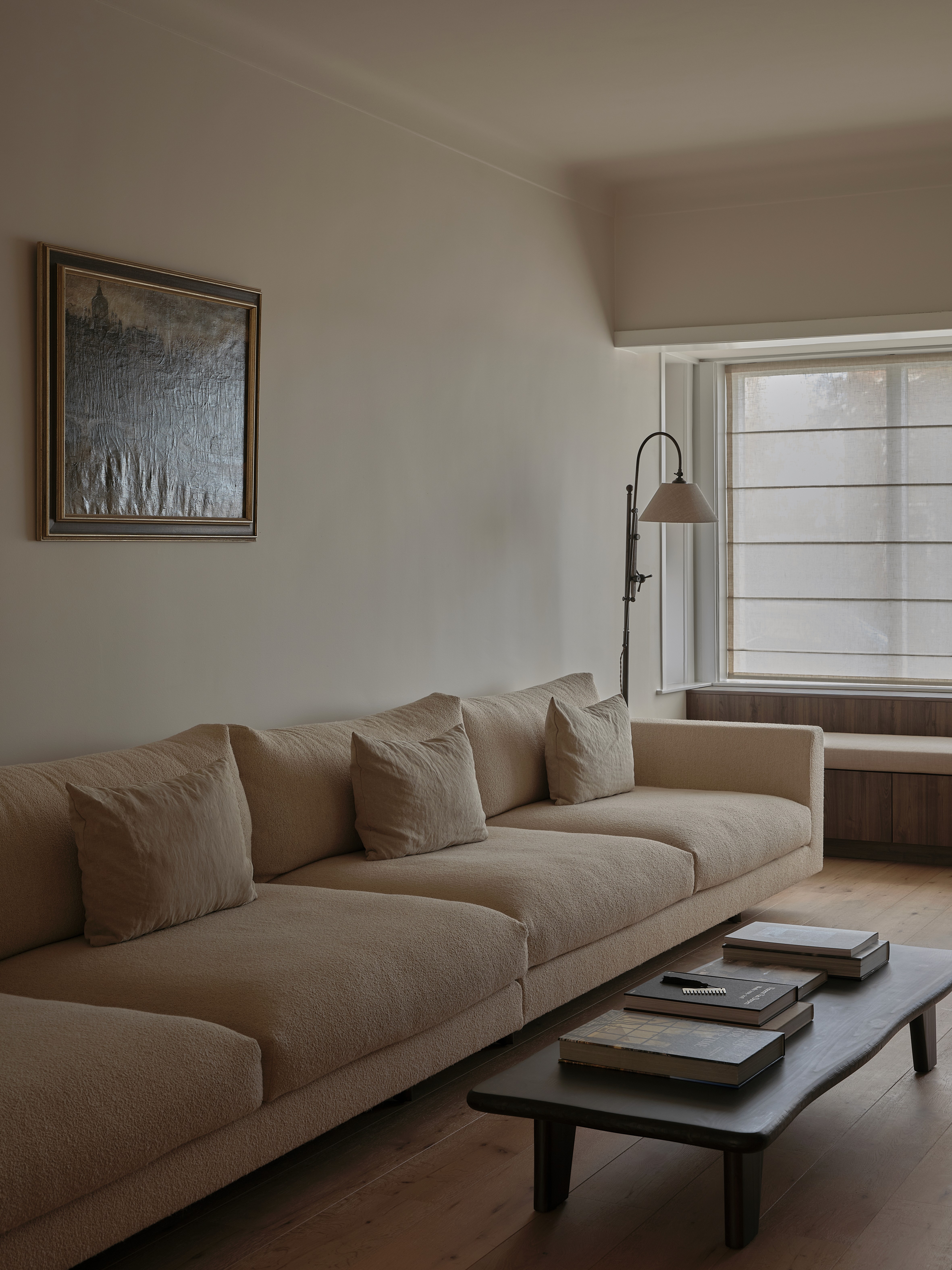 Living room with neutral linen sectional sofa, dark wood coffee table with books, and floor lamp