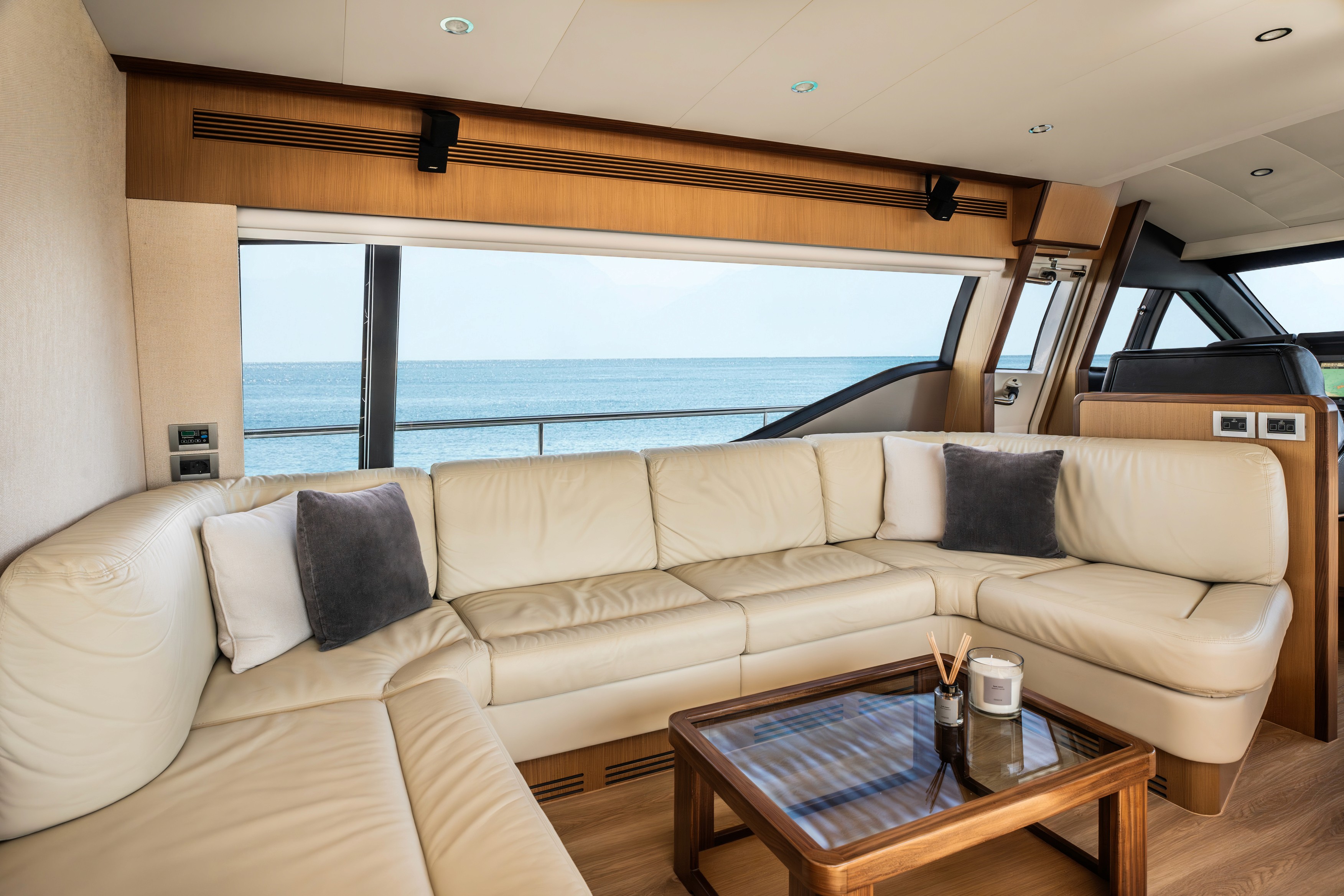 Luxurious main salon of Ferretti 63 yacht featuring cream leather U-shaped seating, wood coffee table, and panoramic windows overlooking calm blue waters.