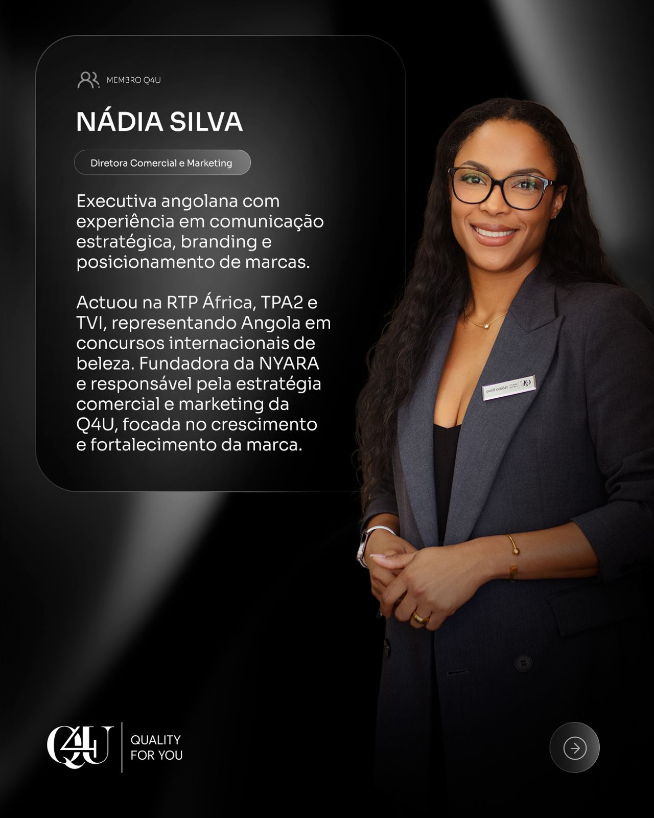 A woman with long wavy hair stands confidently in a bright office, wearing a white shirt and patterned blazer. The setting conveys professionalism.