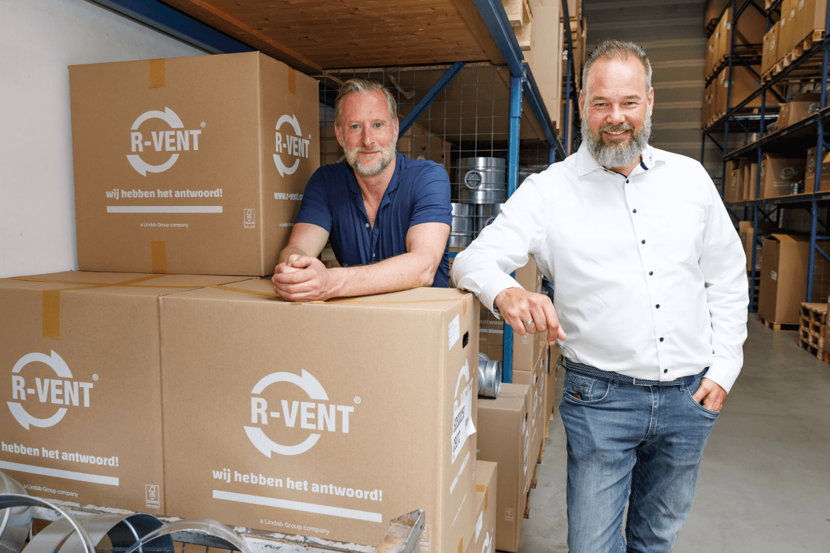 Twee medewerkers van R-Vent naast gestapelde dozen in het magazijn