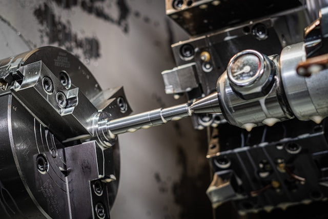 A winding road cuts through rocky terrain, surrounded by patches of green grass and illuminated by sunlight.