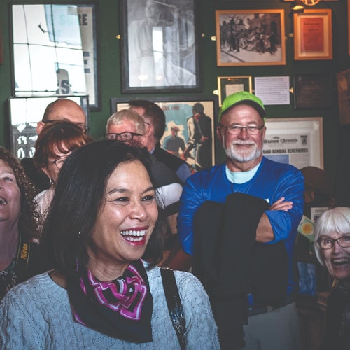 一群人微笑著，笑著，身處於一間有著深綠色牆壁上掛著相框和紀念品的房間裡。