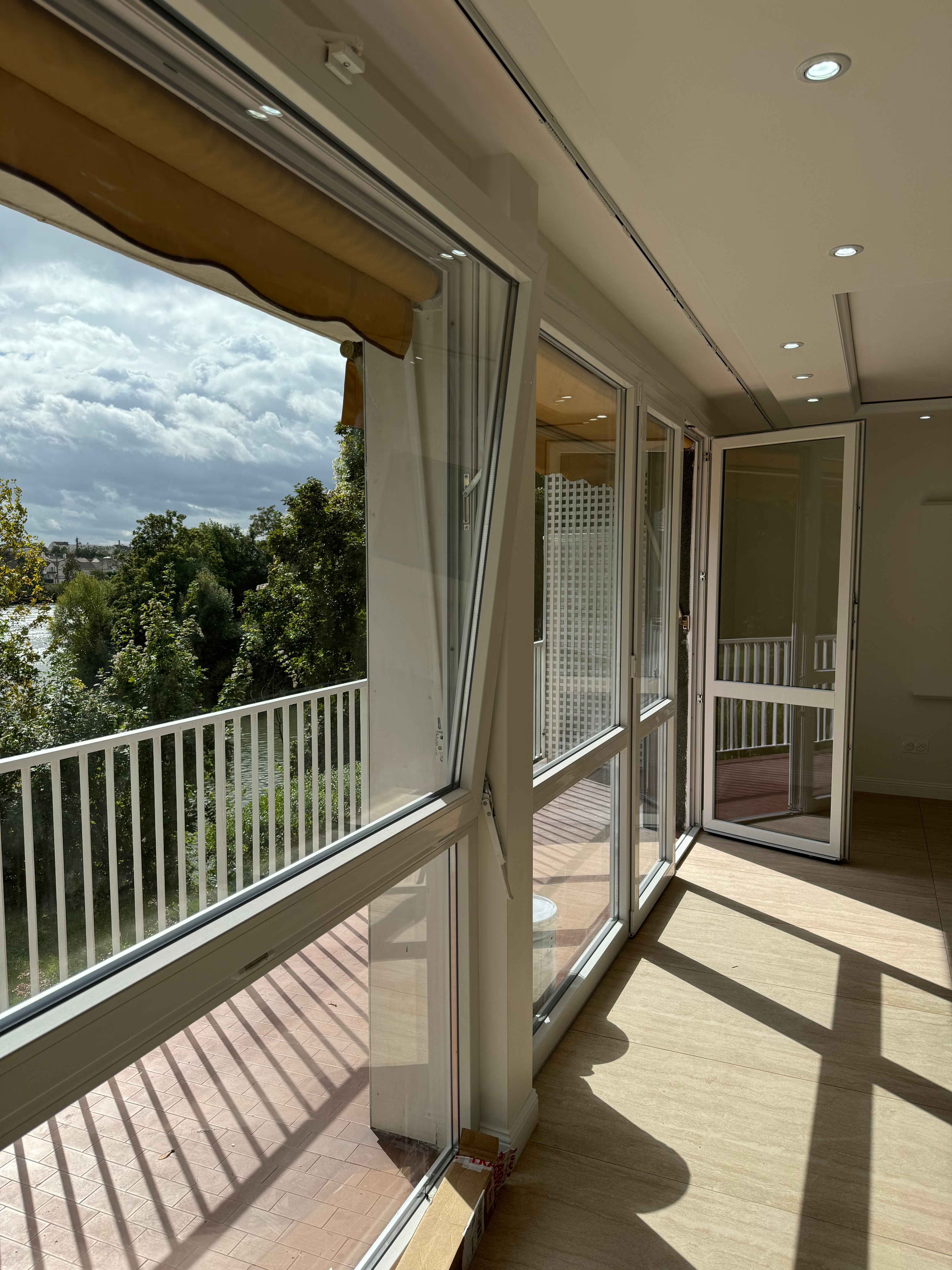 Installation de grandes menuiseries extérieures blanches et baies vitrées ouvrant sur un balcon avec vue dégagée sur la nature et la rivière.