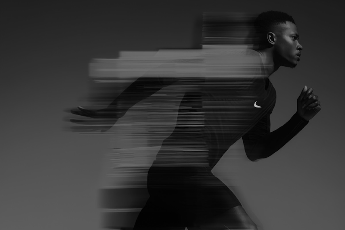 A runner in a sleek athletic outfit is captured in motion, creating a dynamic blur effect that conveys speed and intensity against a dark background.