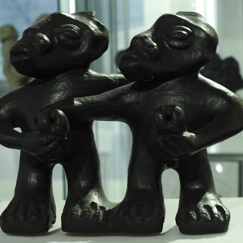 שתי פסלים מופשטים כהים דומים לתאומים עומדים קרוב זה לזה, כל אחד מחזיק דמות קטנה, על רקע מטושטש.