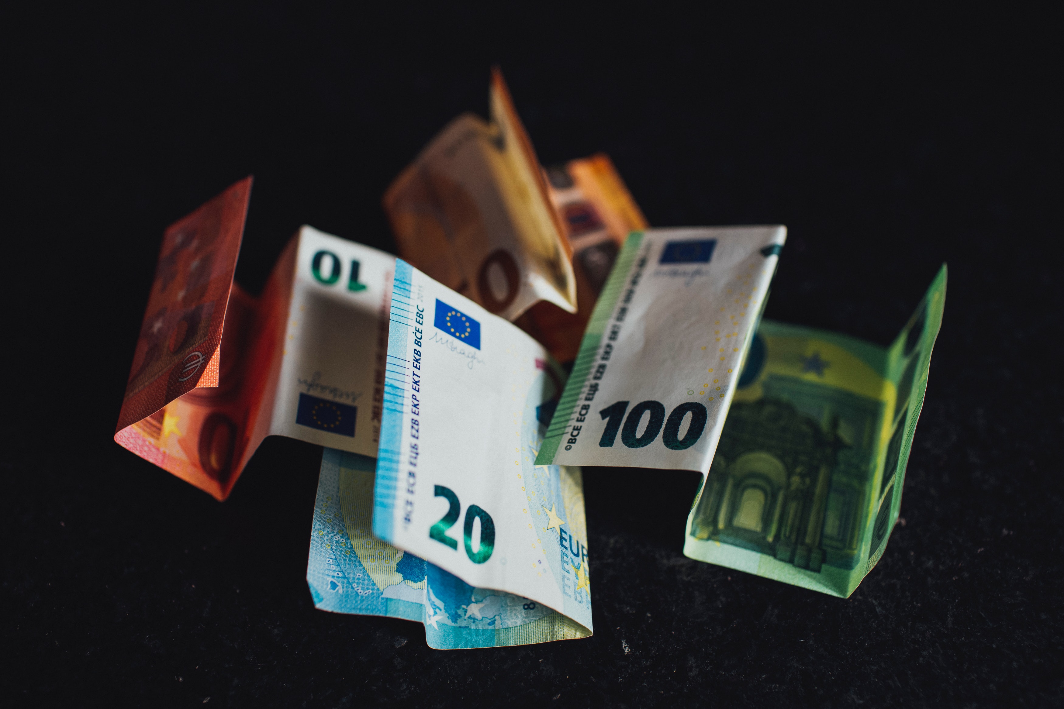 Een verzameling van verschillende kleurrijke bankbiljetten in diverse denominaties, verspreid over een donkere ondergrond.
