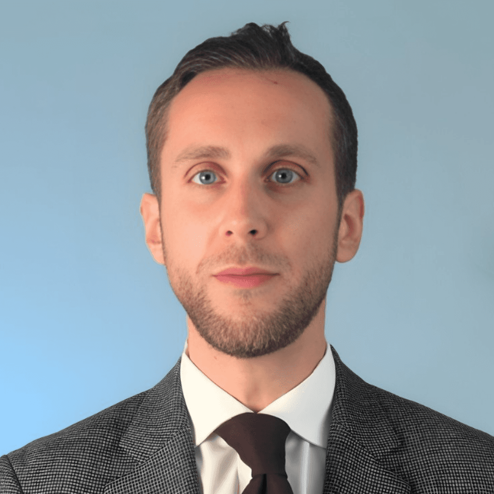 A woman with short curly hair wearing a black t-shirt looks into the camera.