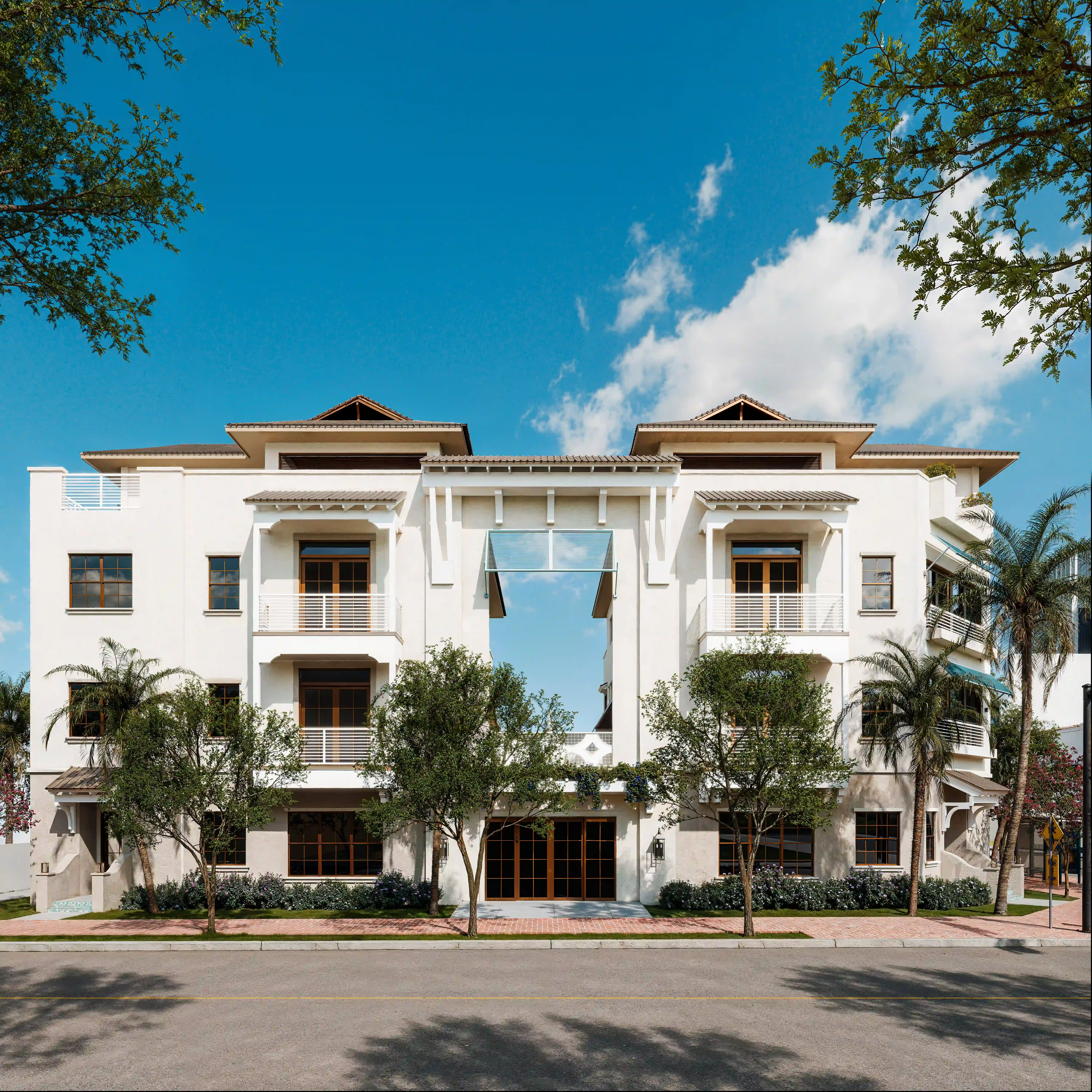Front view of a symmetrical white three-story apartment building with balconies and a central archway, framed by palm trees under a bright blue sky.