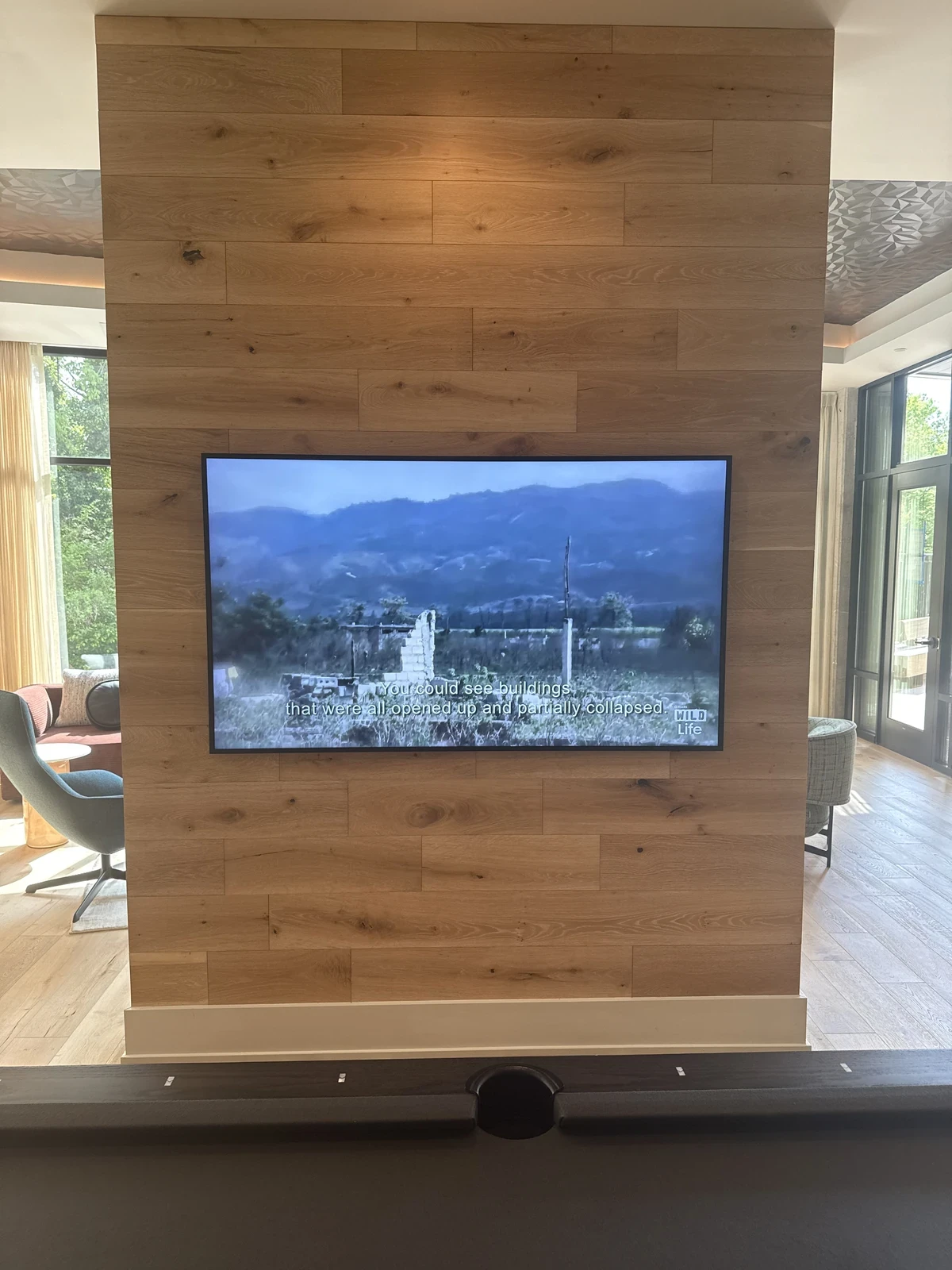 Television mounted on a wood feature wall in a room with natural daylight.