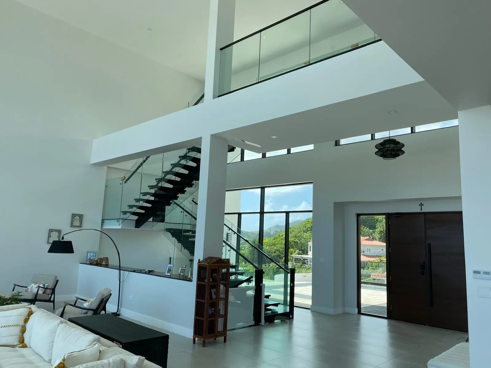 Entry and stair hall at The Hill Residence in St. Lucia designed by Atelier International, with a floating steel staircase, glass balustrades, and a double-height mezzanine.