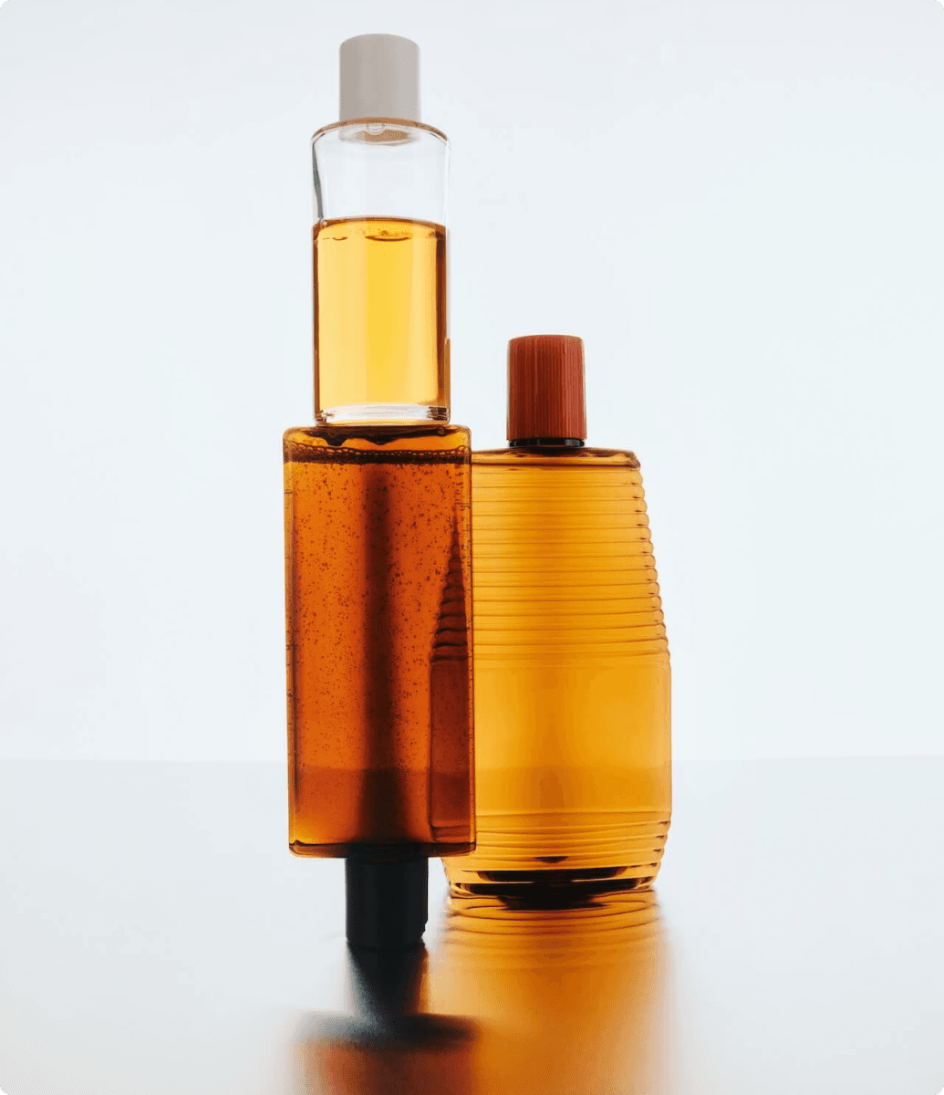 A set of amber-colored bottles with various designs, standing on a reflective surface, capturing light beautifully against a white background.