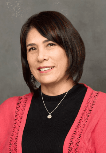 Stylish person with pastel pink hair wearing round sunglasses and a yellow floral shirt, posing in profile against a bright turquoise background.