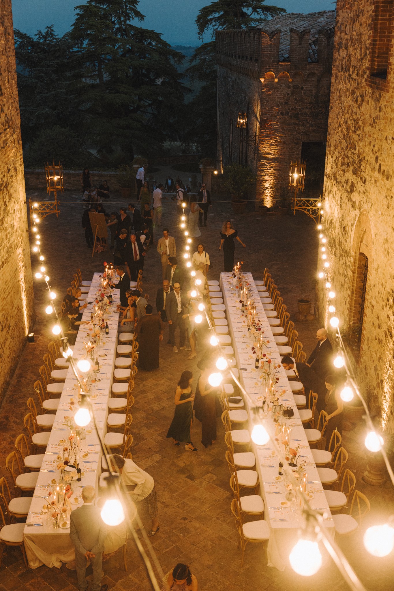 Lunghe tavolate illuminate al tramonto nel cortile del Castello di Tabiano, ricevimento matrimoniale di Eline e Antoine