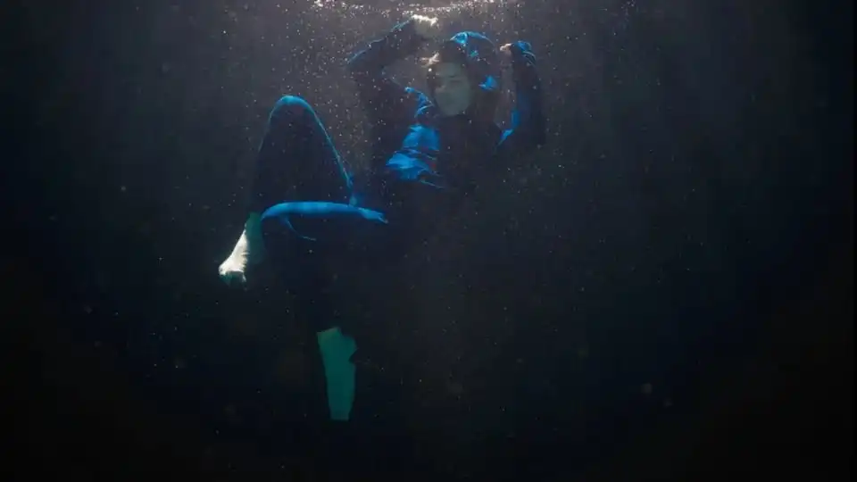 Person floating underwater in dark blue light.