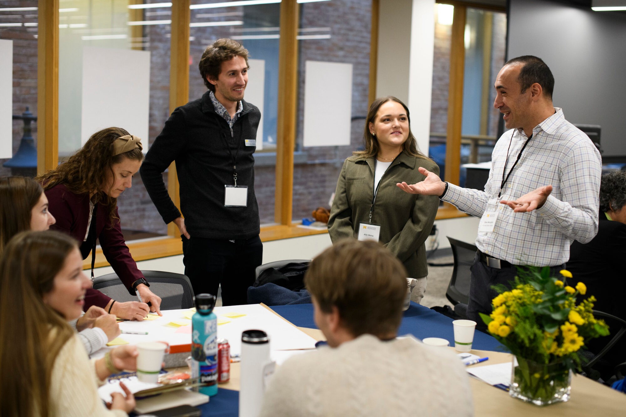 Group of four people in a meeting, discussing with papers and a flower vase on the table. Engaged conversation.