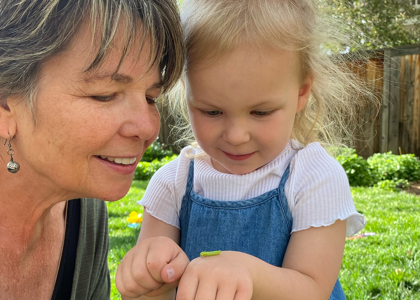 Grandmother and grandaughter outdoors looking at green at green caterpillar 