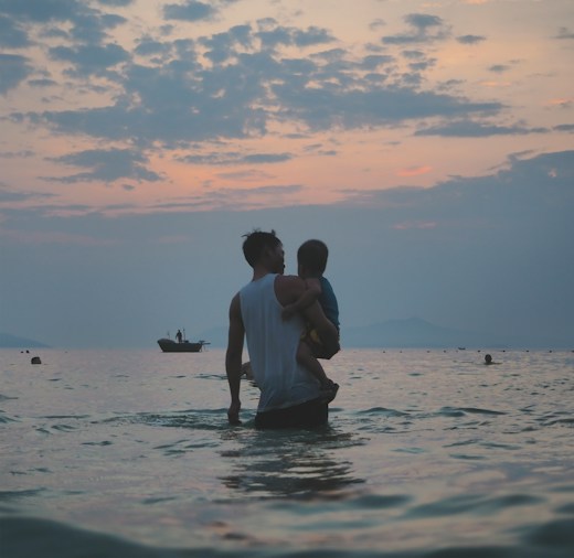 Padre con su hijo en brazos en el mar al atardecer: seguros de accidentes, decesos y viaje para familias