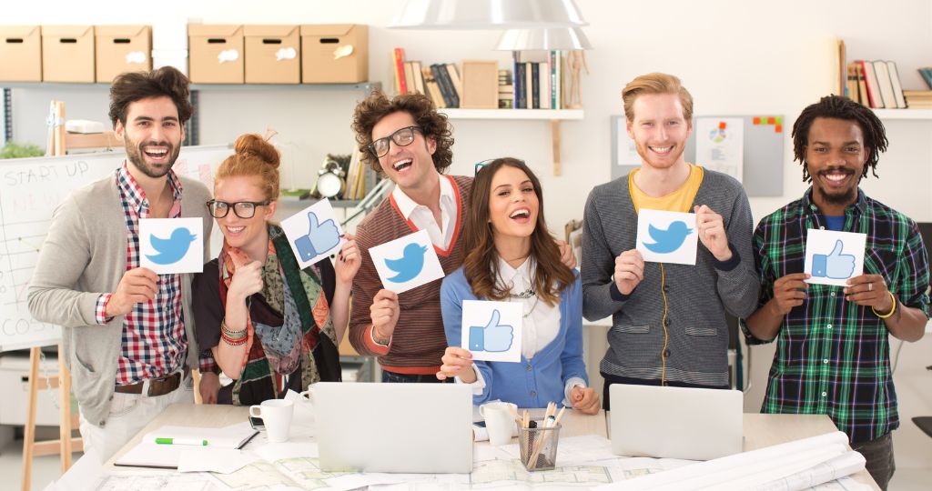 Team of social media marketers holding Twitter and Facebook icons, smiling in an office setting.