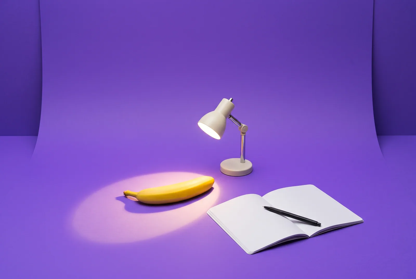 A banana under a bright desk spotlight beside an open blank notebook, a playful QUITTR vs Ever Accountable comparison