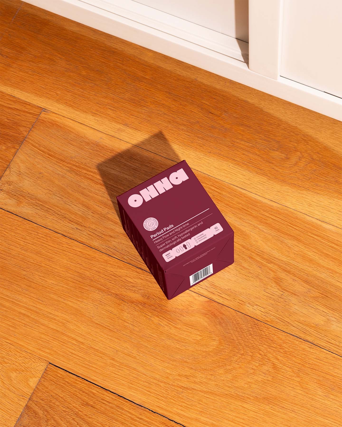 Burgundy product box on wooden floor displaying period pad packaging design