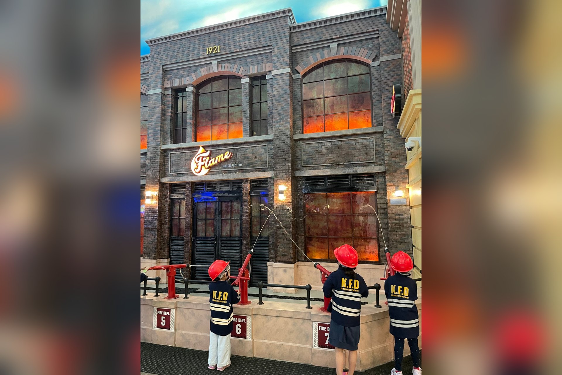 Des enfants en tenue de pompier arrosent la façade d'un immeuble de la ville miniature de KidZania Doha