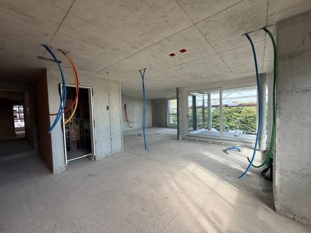 Rohbau einer Wohnung mit Sichtbeton, offen liegenden Leitungen und einem grossen Fensterband.