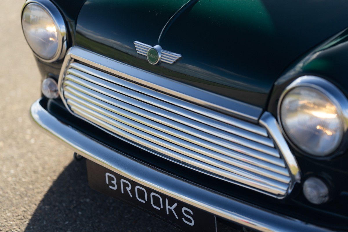 Close-up of a classic car's grille, featuring chrome accents and a glossy dark green paint finish.