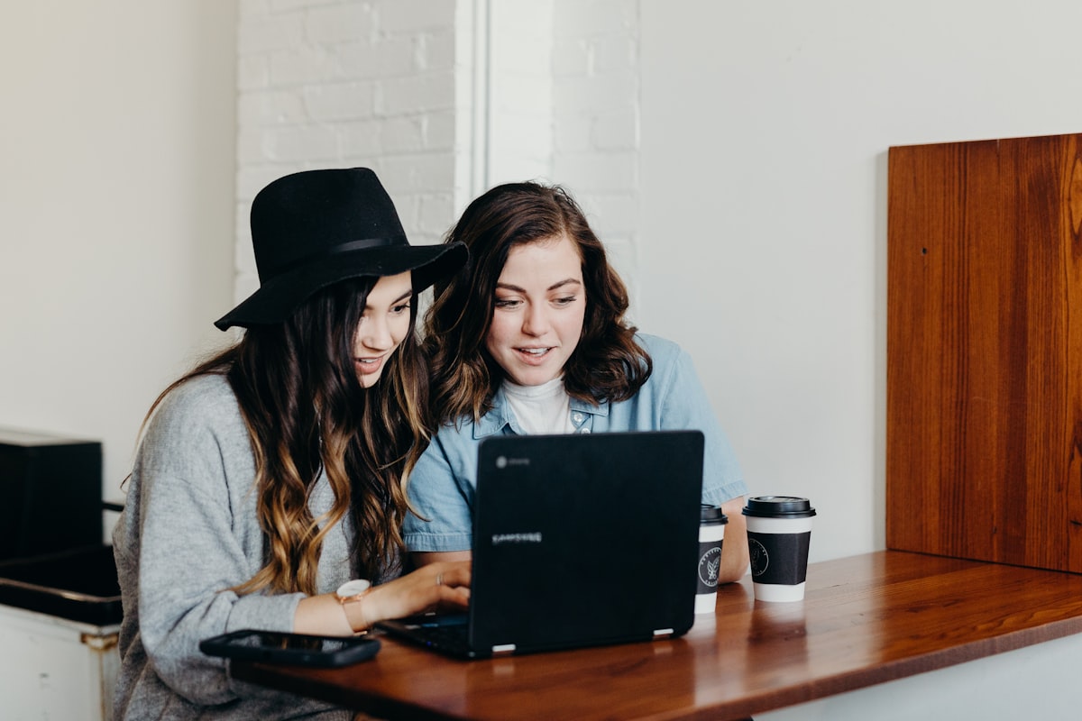 Two friends sitting at a table planning a group trip together on a laptop