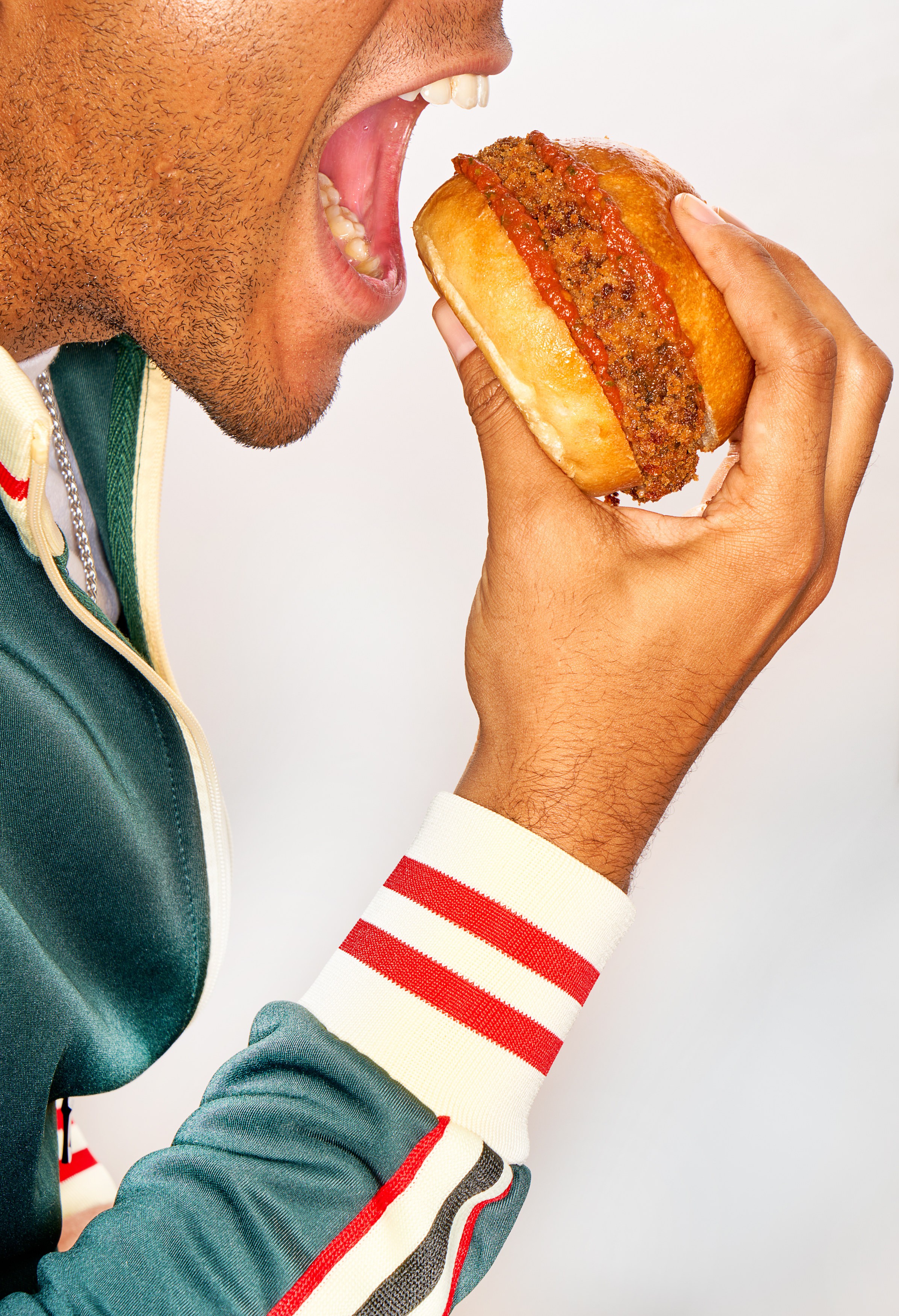 Talent in a green tracksuit bringing a Kernel burger toward his mouth