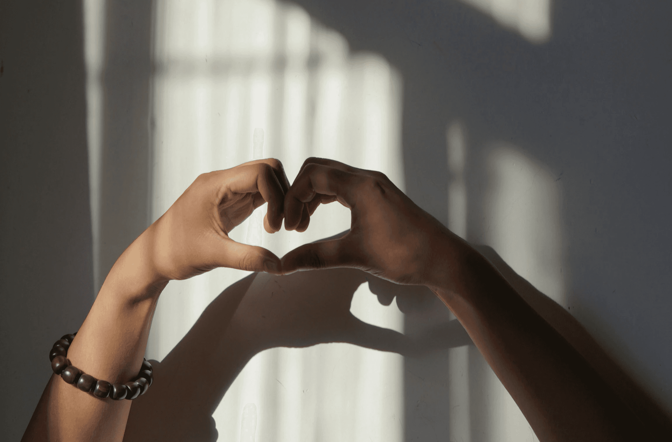 Hands forming a heart shape with window light.