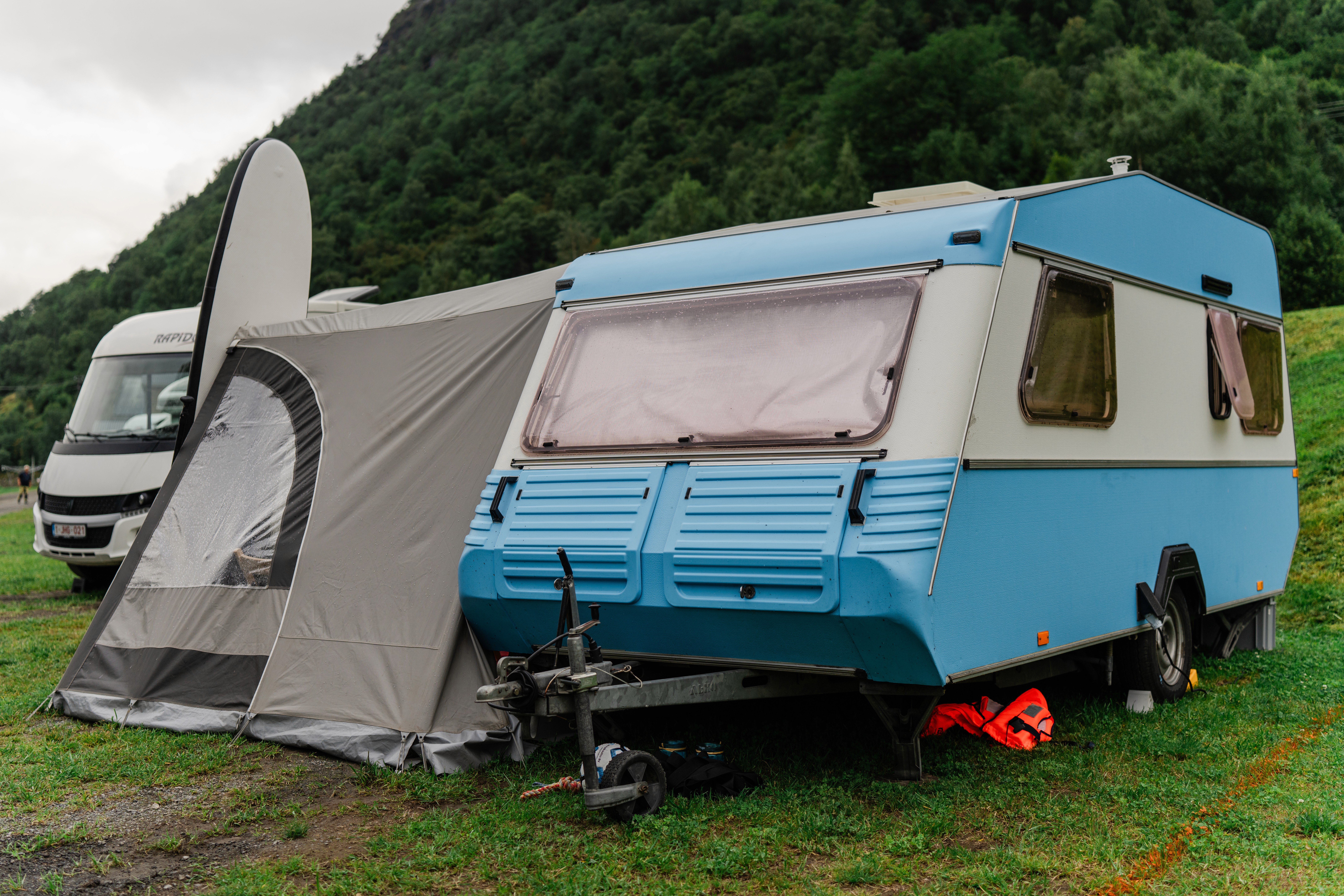 A blue camper and awning stand on grass beside the lake.