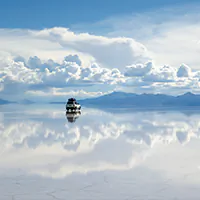 Pôr do sol refletido no Salar de Uyuni, com céu alaranjado e espelho d’água na Bolívia