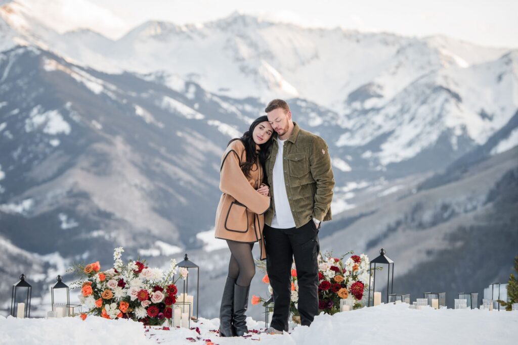 Couple embracing beside flowers in a snowy mountain setting