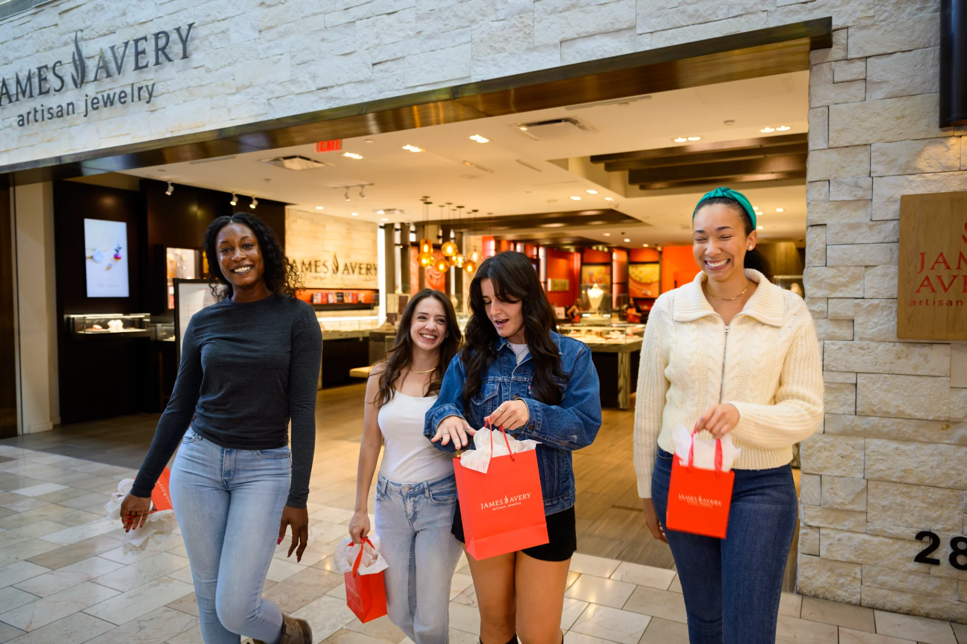Four friends walking out of James Avery Artisan Jewelry carrying red shopping bags