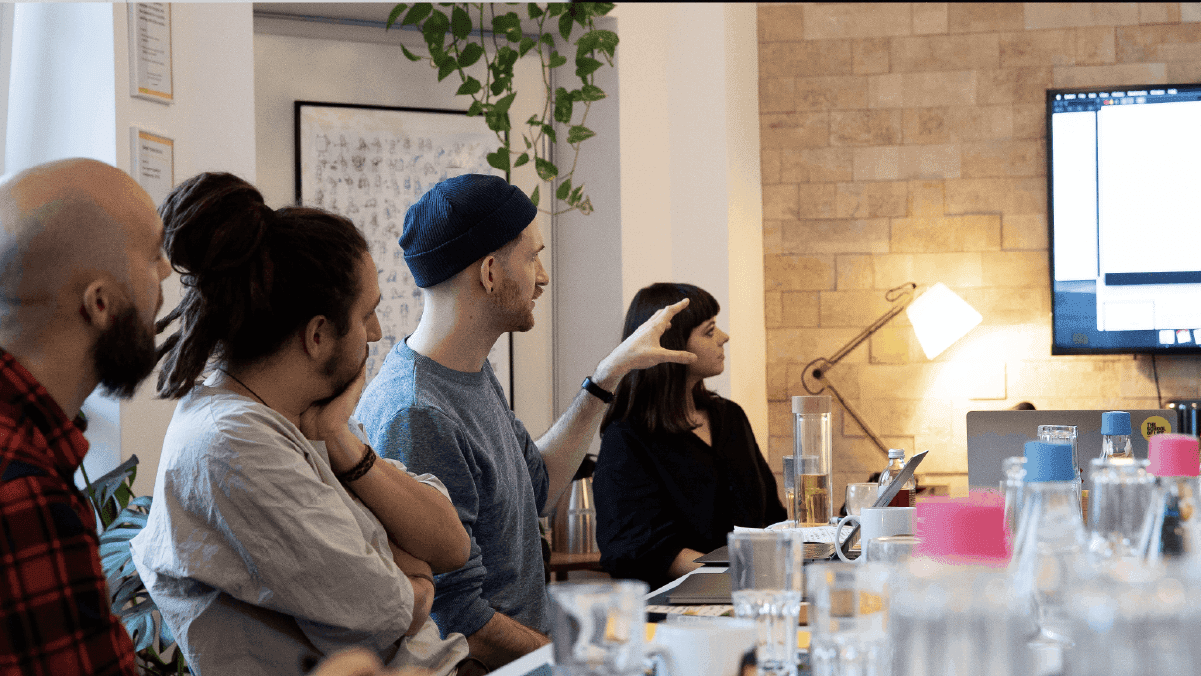Design team seated at a table during a UX workshop with a presentation screen in the background