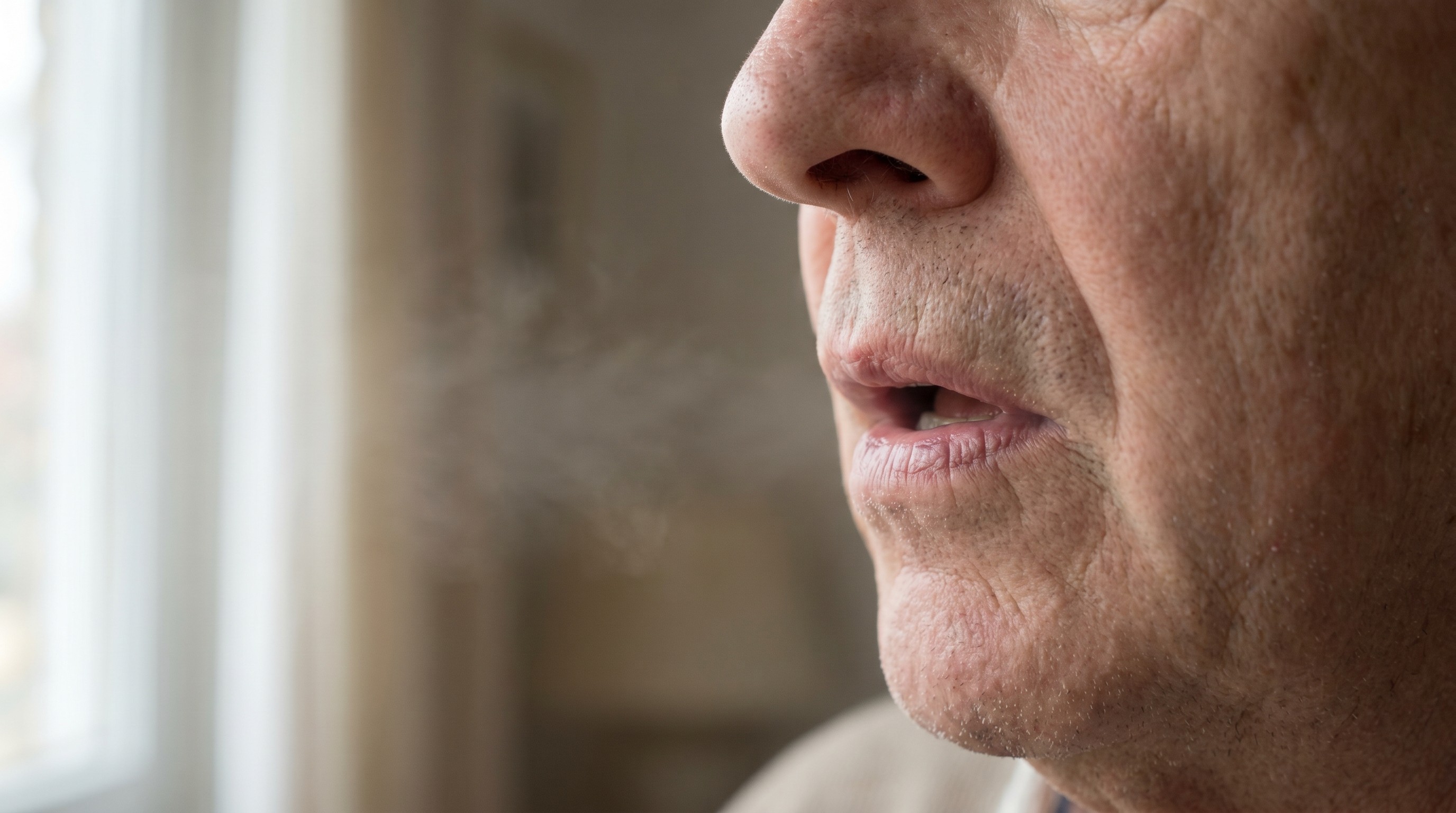 Close-up of an older adult's mouth slightly open while breathing in cool air