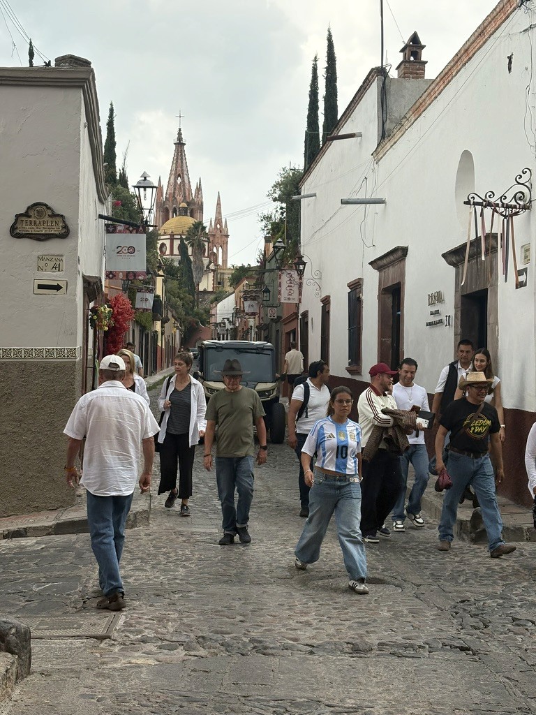 Pedestrians on a cobblestone street with the Parroquia in the background