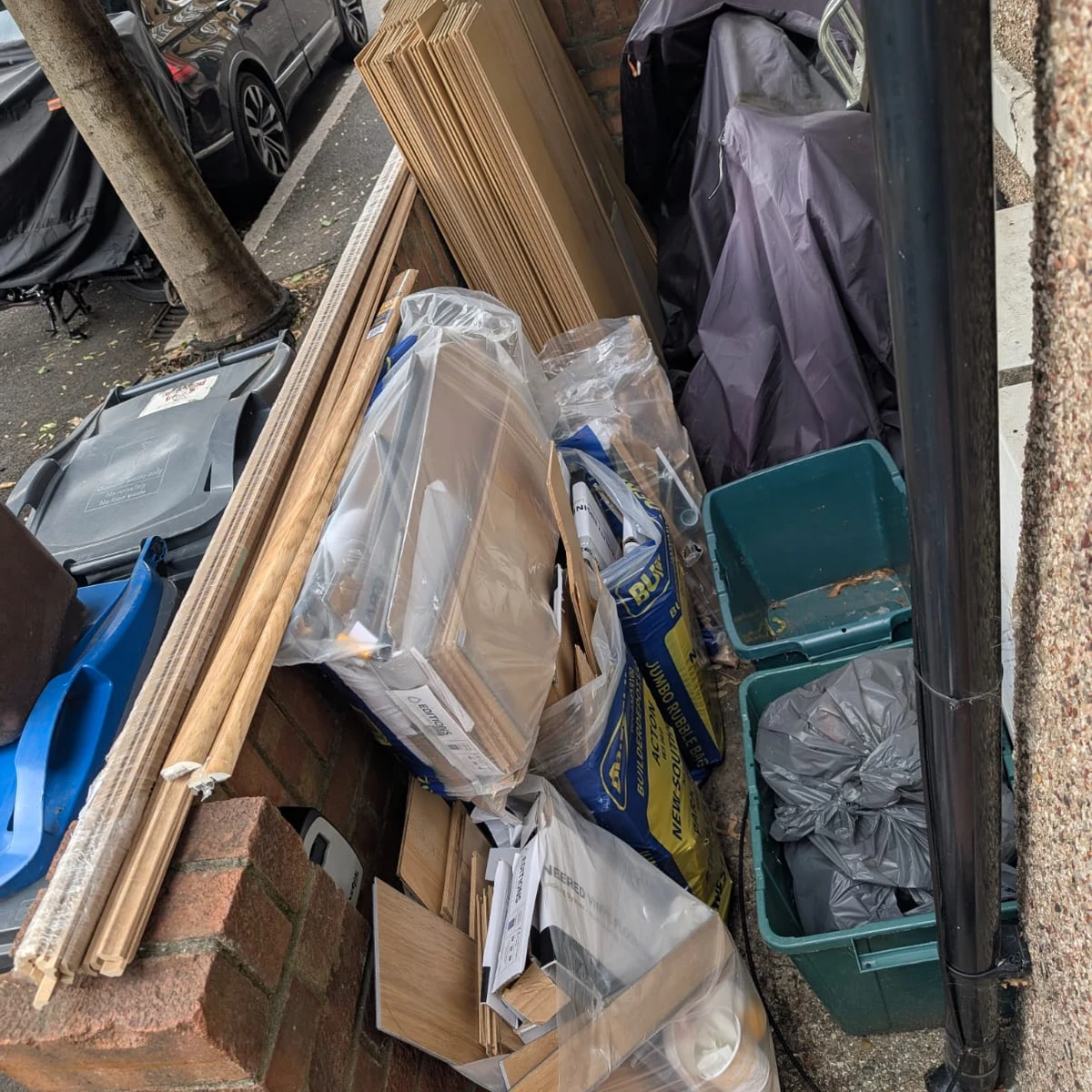 Builders waste and laminate flooring offcuts stacked in a side passage during a Clapham rubbish clearance