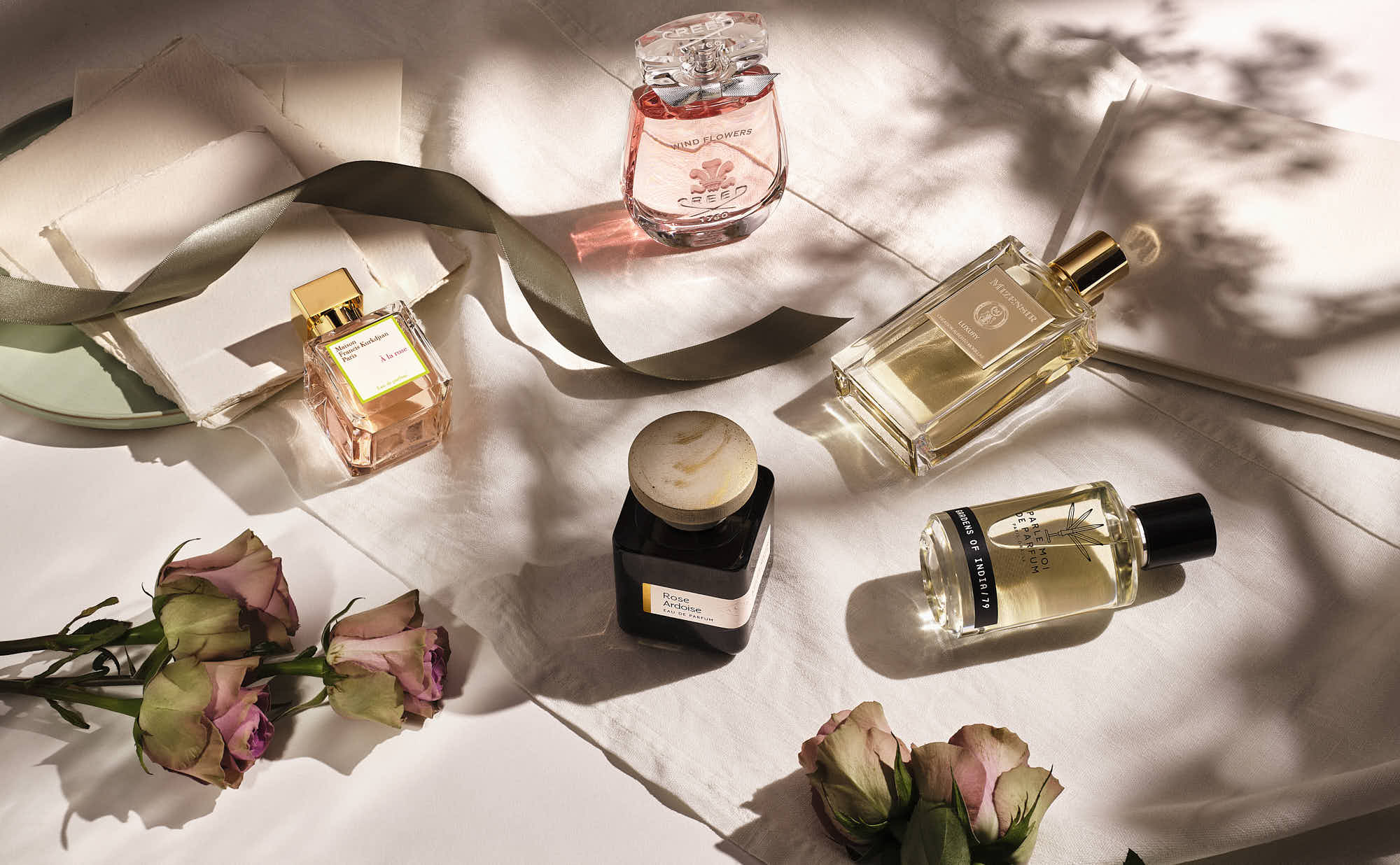 A flat lay of various perfume bottles and beauty products arranged on a soft, light-colored background.