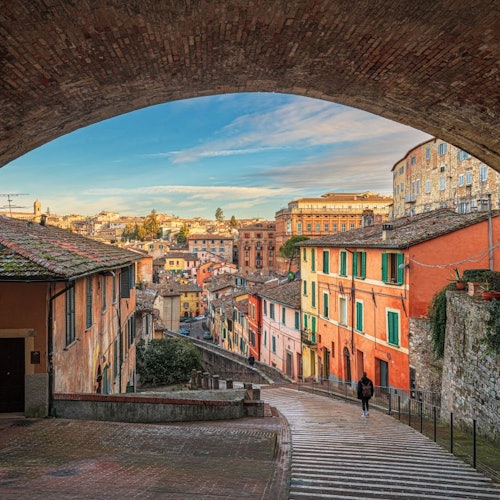 A scenic view of a European town with colorful buildings, seen through a stone archway, under a clear sky.