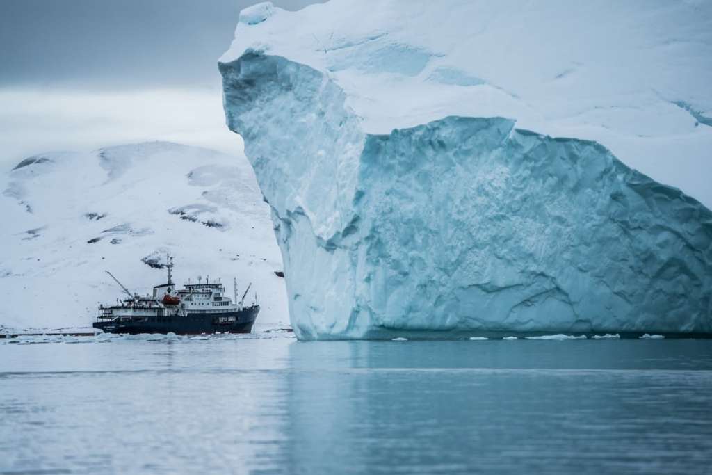 Icebreaker boat next to huge iceberg, Svalbard