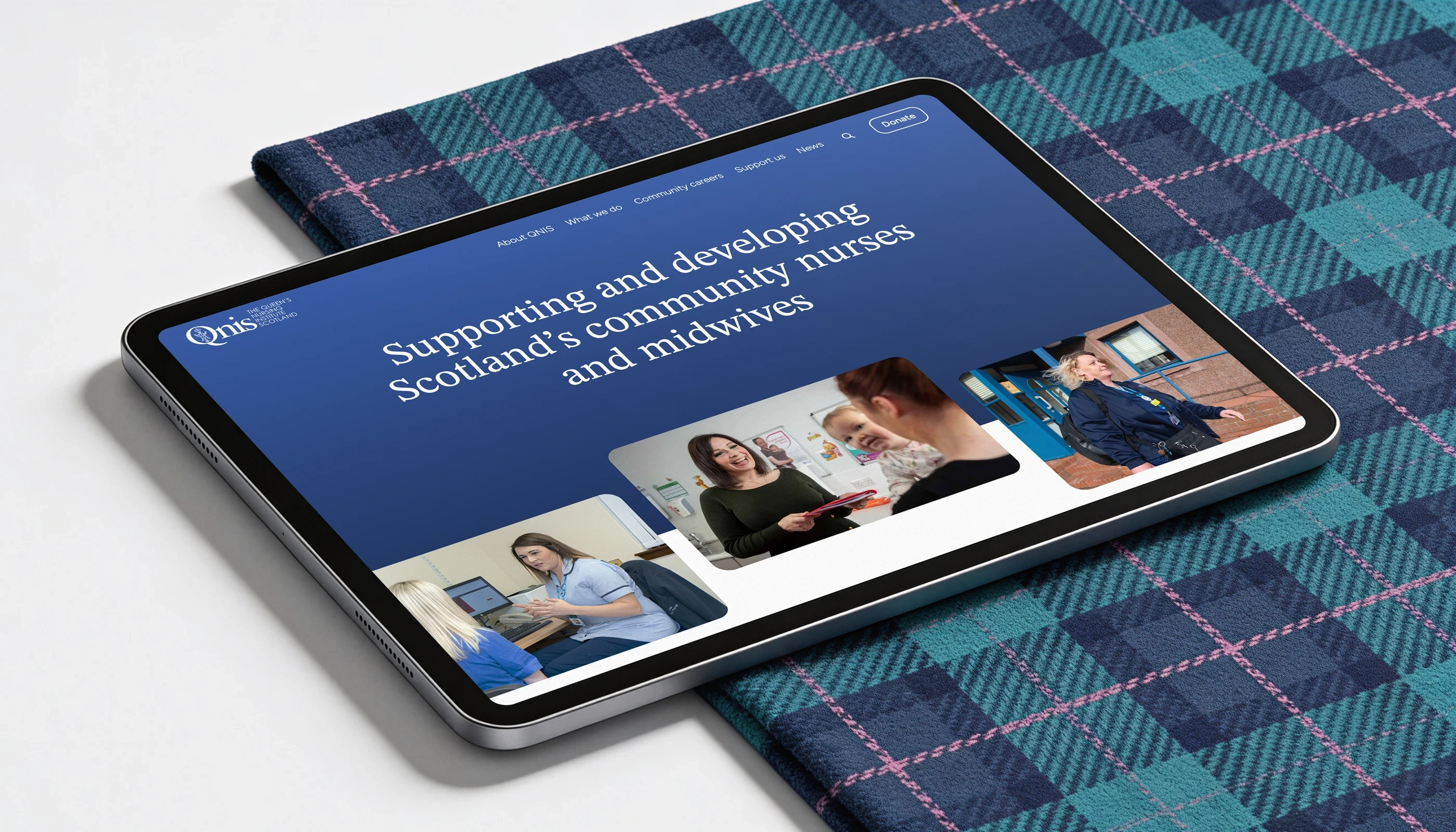 Tartan on a table with an iPad on top of it displaying The Queen's Nursing Institute Scotland's website