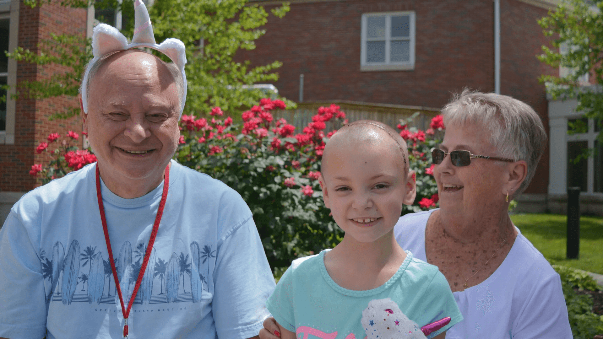 Smiling child sitting outdoors with two older adults, sharing a joyful moment in a garden setting