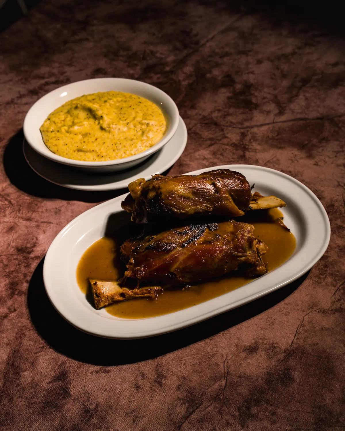 Three people are carefully removing a fresh loaf of artisanal bread from a rustic, wood-fired brick oven, with flames visible inside.