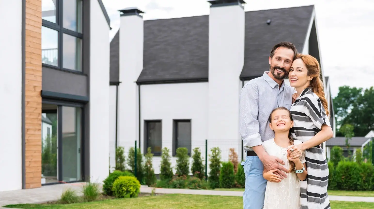 A smiling family stands together in front of their newly built modern home, symbolizing the joy and fulfillment of achieving homeownership through a new construction loan with Chris Lewis Home Loans.