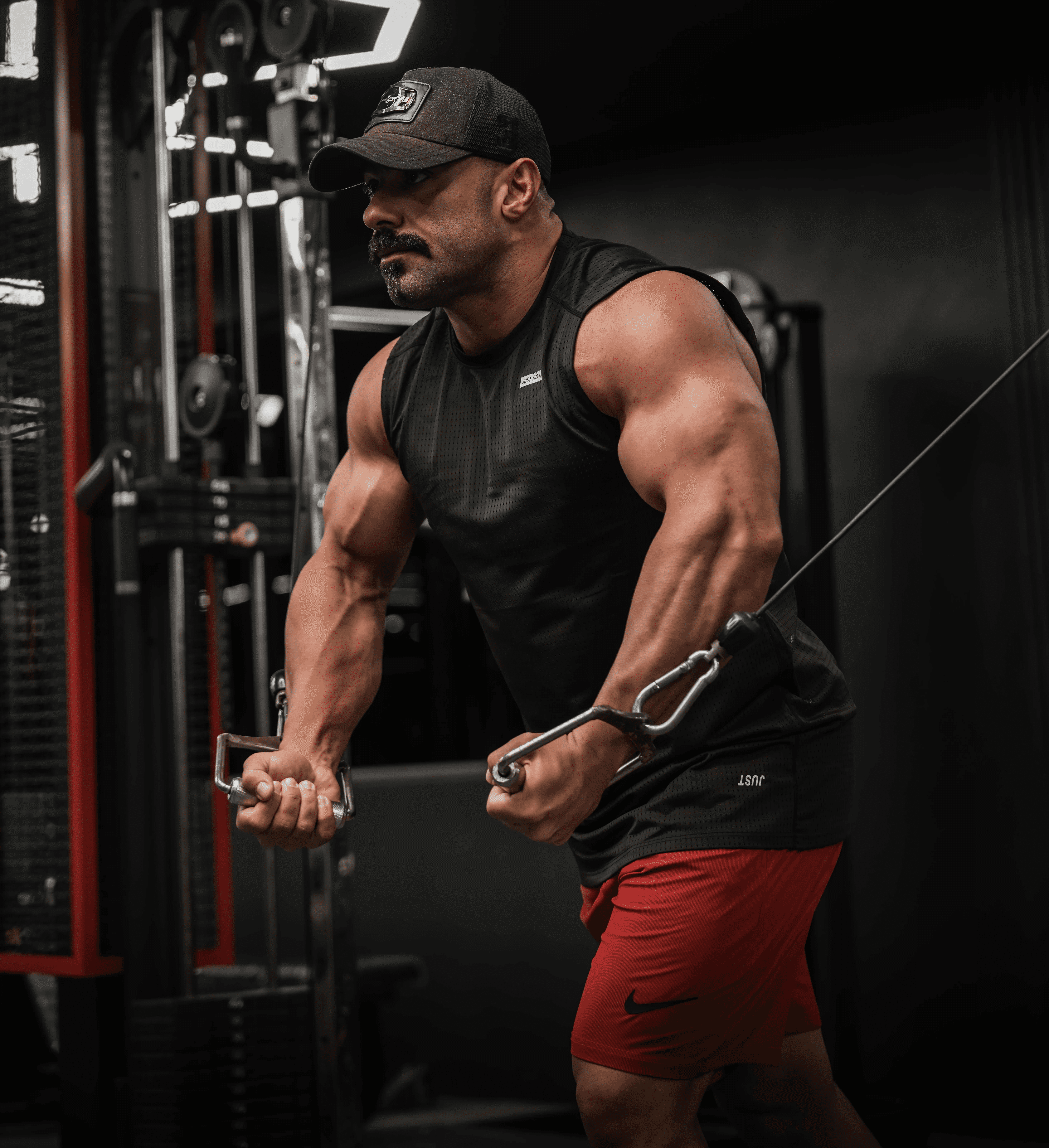 A muscular man with defined abs and tattoos is intensely lifting dumbbells in a dimly lit gym, showcasing a focused strength workout routine.